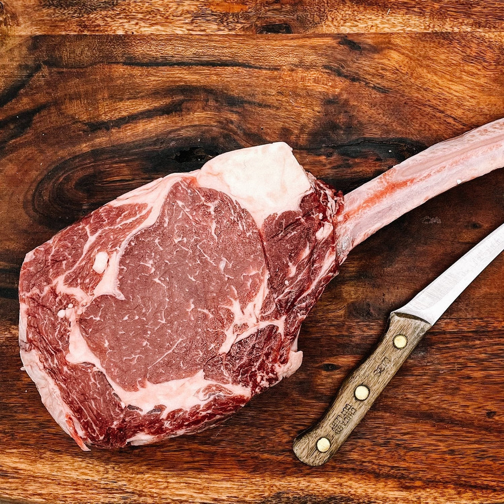 Creamery Creek Dry Aged Tomahawk on a cutting board with a knife nearby