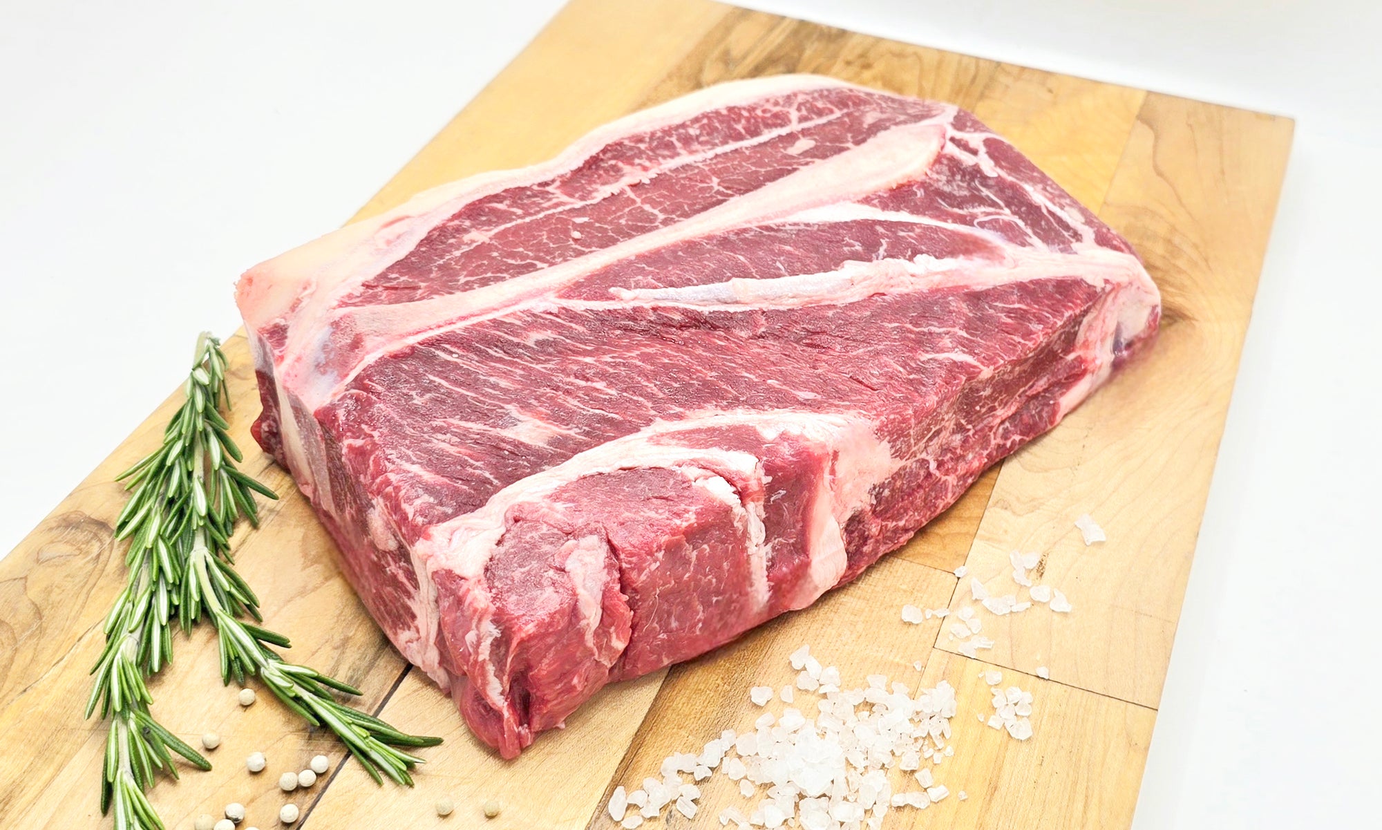 Raw chuck roast on a wooden cutting board with rosemary and salt