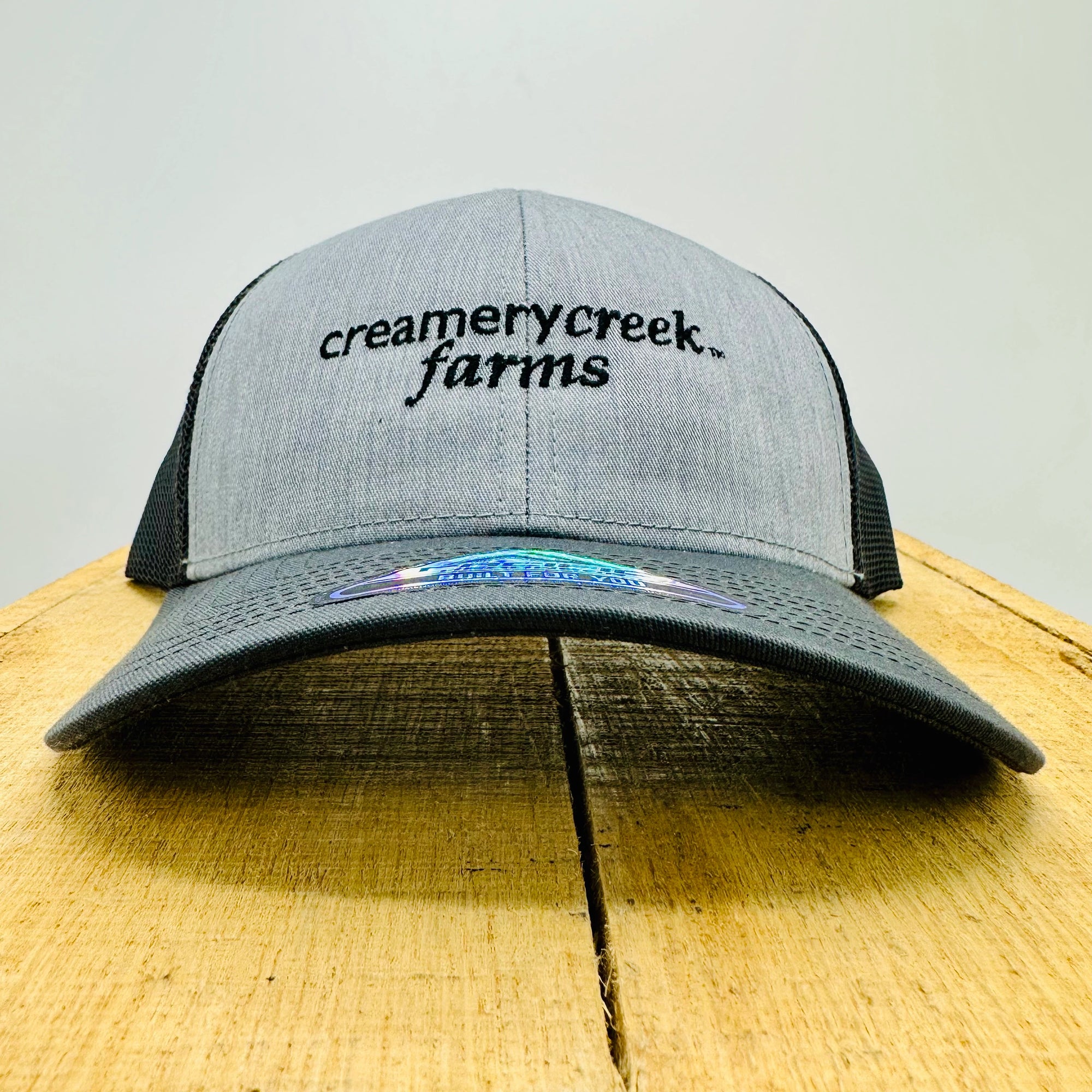 Gray and black cap with 'Creamery Creek Farms' logo on a wooden surface.
