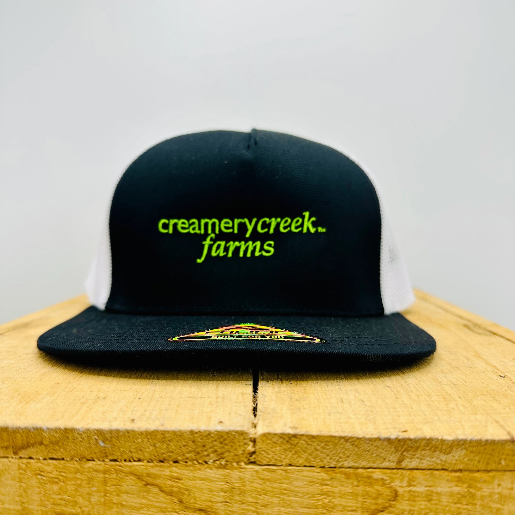 Black cap with 'creamerycreek farms' text on a wooden surface