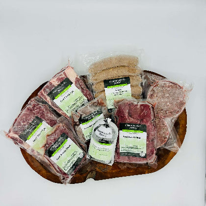 Assorted packaged meats on a wooden board with 'Creamery Creek Farms' labels.