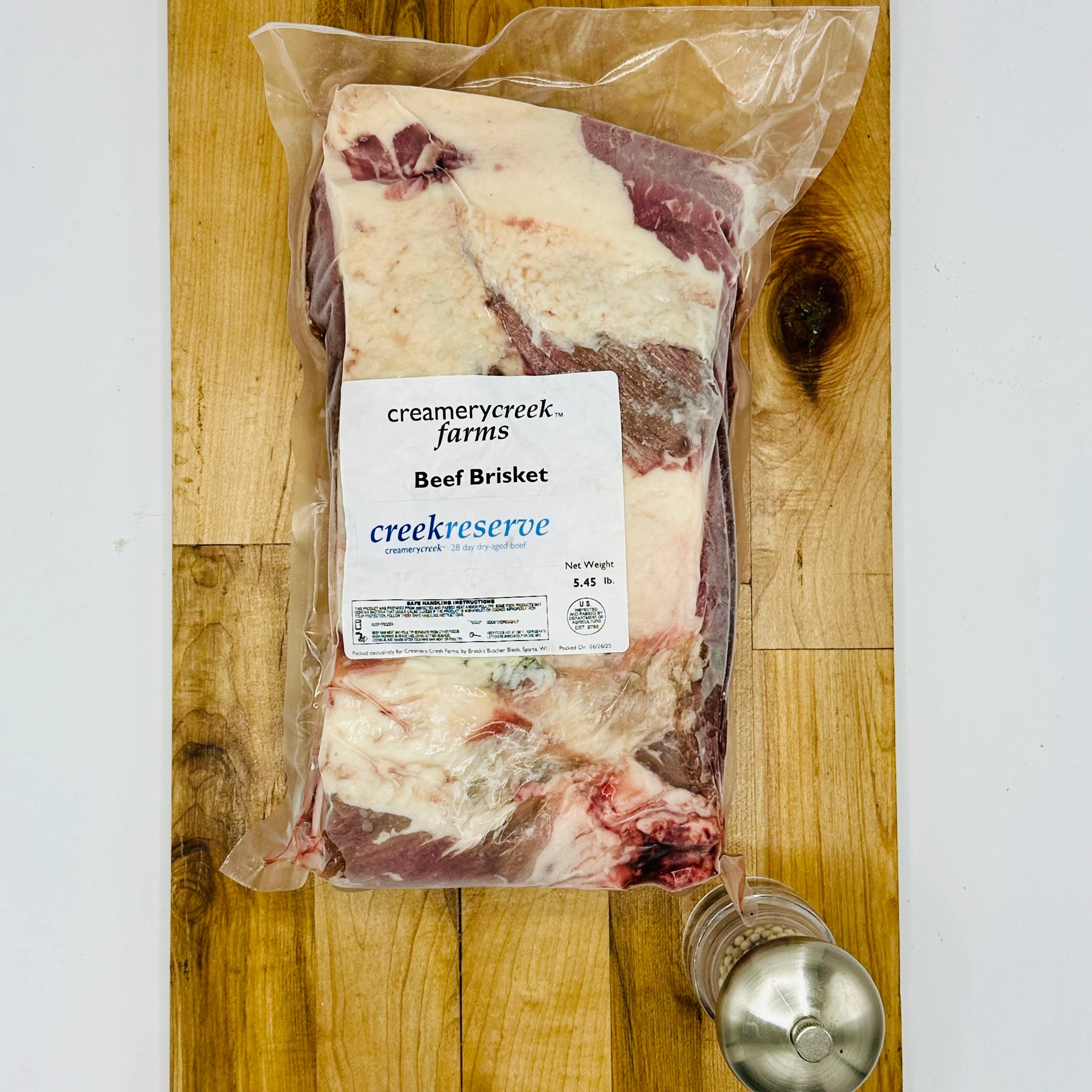 Packaged beef brisket from Creamery Creek Farms on a wooden cutting board.