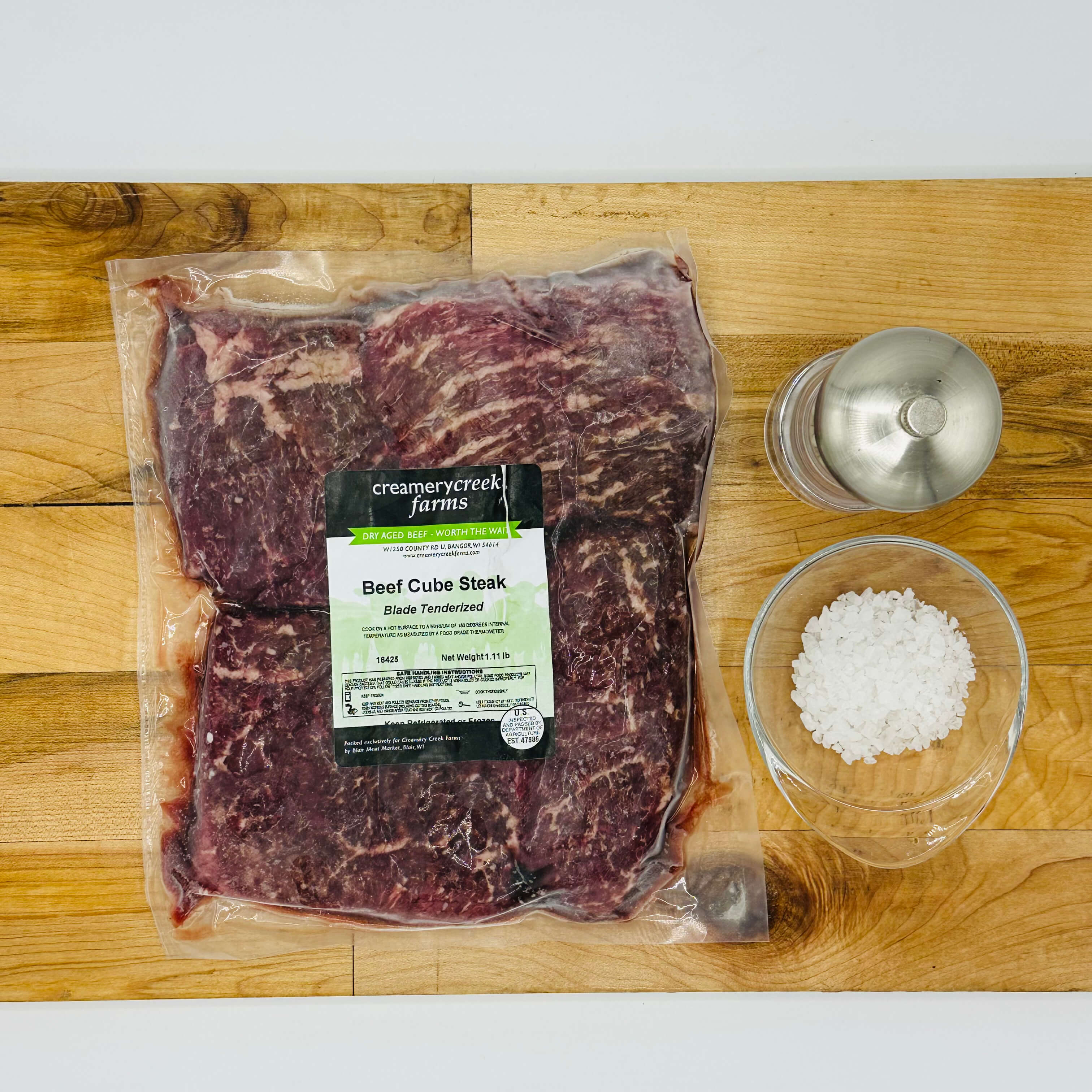 Packaged beef cube steak with a salt container on a wooden cutting board