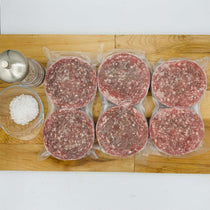 Six packages of ground meat on a wooden cutting board with salt and pepper shakers.