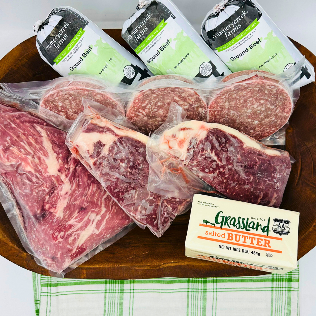 Assorted ground beef packages and a stick of Grassland Creamery butter on a wooden board.
