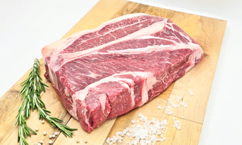 Raw chuck roast on a wooden cutting board with rosemary and salt