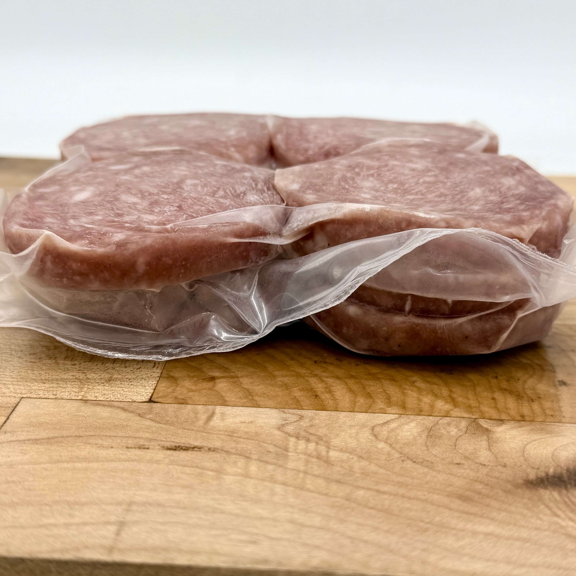 Two pieces of raw meat in clear plastic wrap on a wooden cutting board.