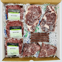 Assorted raw meat packages including steaks and ground beef in a box with Creamy Creek Farms branding.