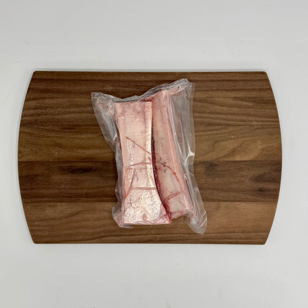 Packaged canoe cut marrow bones on a wooden cutting board with a white background