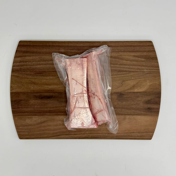 Packaged canoe cut marrow bones on a wooden cutting board with a white background