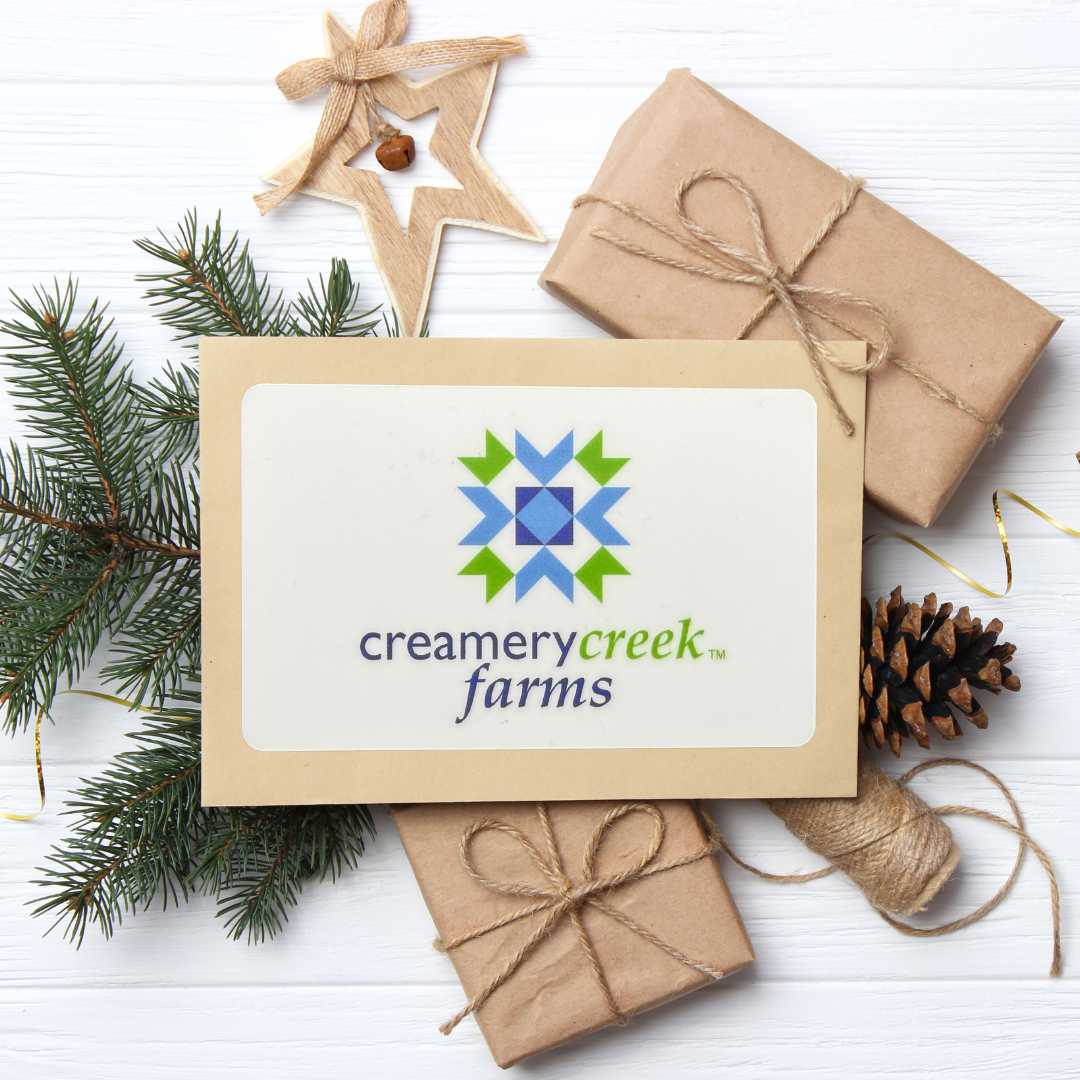 Gift card with Creamery Creek Farms logo surrounded by Christmas decor on a white surface