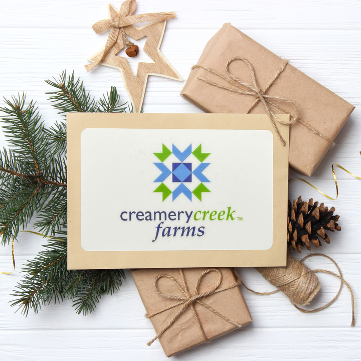 Gift card with Creamery Creek Farms logo surrounded by Christmas decor on a white surface