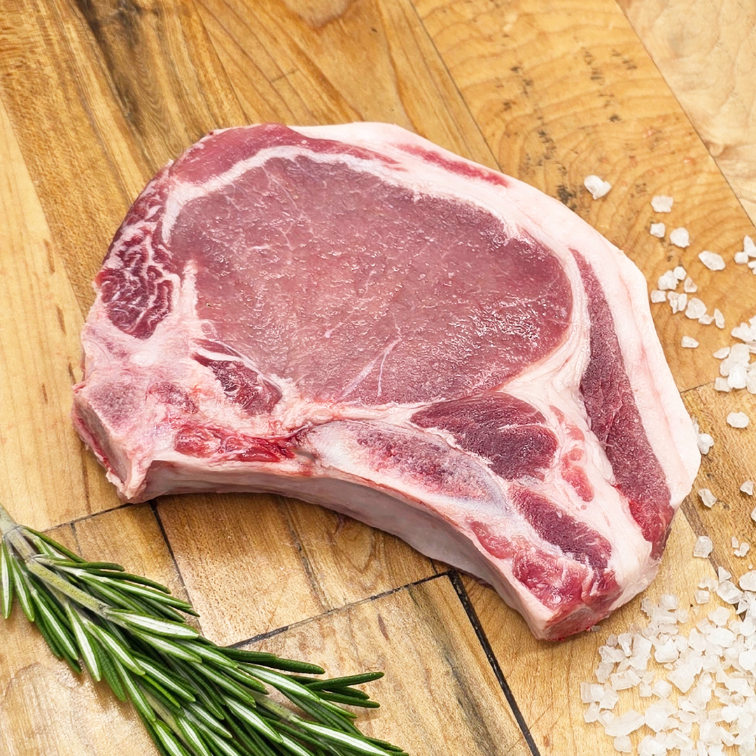 Raw ribeye steak on a wooden cutting board with rosemary and salt.