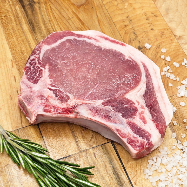 Raw ribeye steak on a wooden cutting board with rosemary and salt.