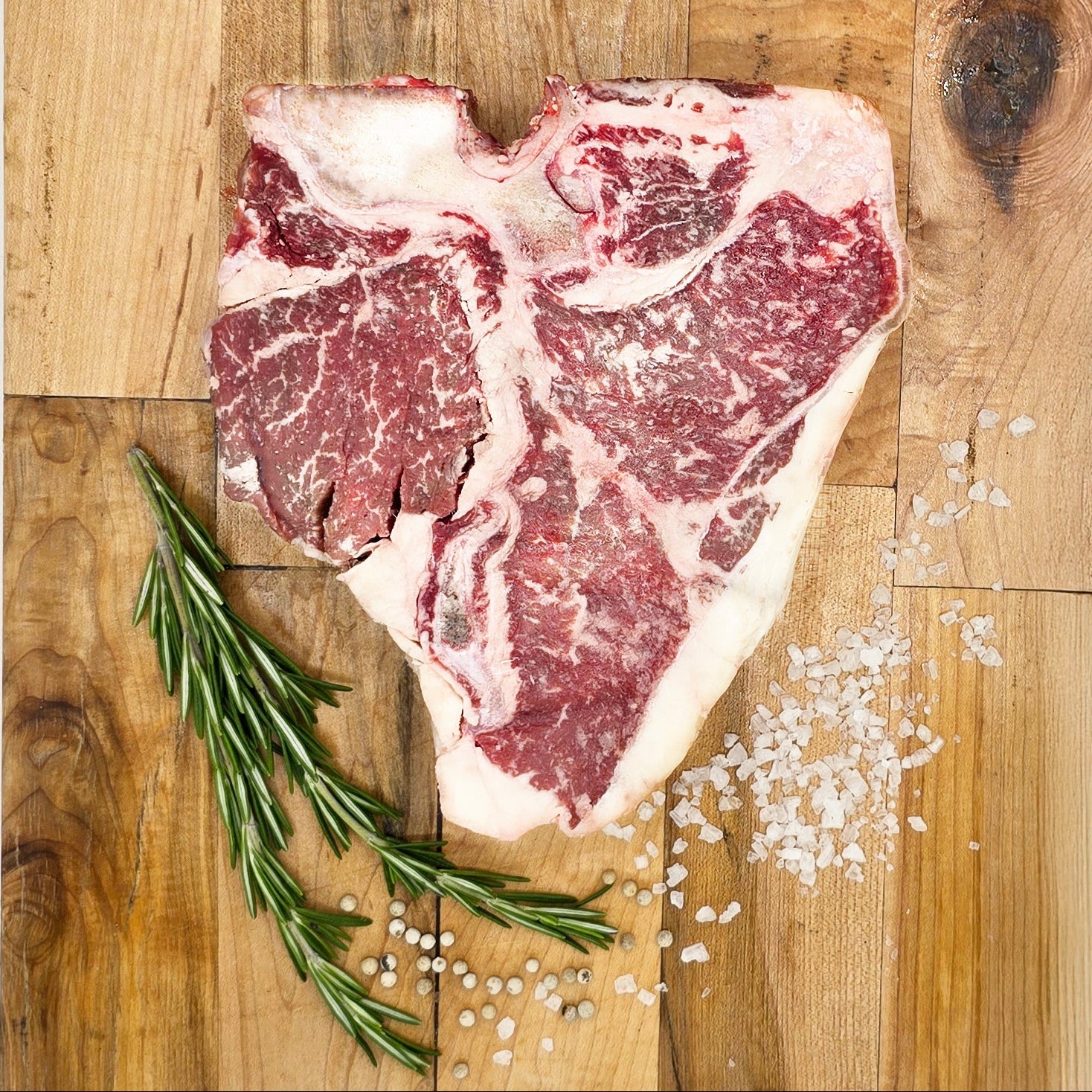 Raw steak on a wooden cutting board with rosemary and salt