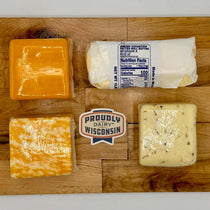 Three types of cheese and rolled butter on a wooden cutting board with a 'Proudly Dairy Wisconsin' label.