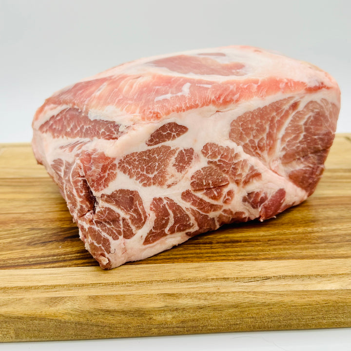 A raw marbled cut of Duroc Pork Boston Butt with pink-red muscle and white fat, resting on a wooden cutting board against a light gray background.