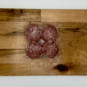 Four packages of salami on a wooden cutting board