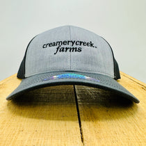 Gray and black cap with 'Creamery Creek Farms' logo on a wooden surface.