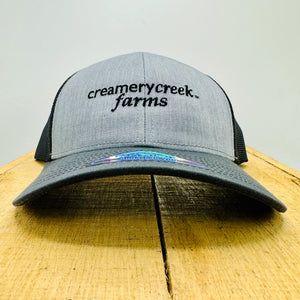Gray and black cap with 'Creamery Creek Farms' logo on a wooden surface.