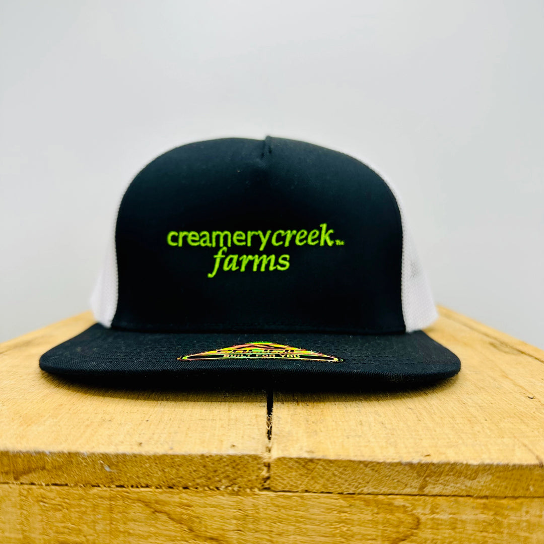 Black cap with 'creamerycreek farms' text on a wooden surface