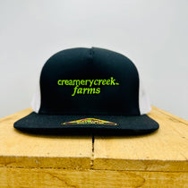 Black cap with 'creamerycreek farms' text on a wooden surface