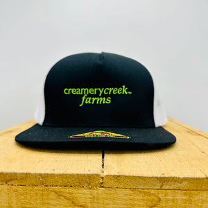 Black cap with 'creamerycreek farms' text on a wooden surface