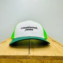 White and green cap with 'Creamery Creek Farms' logo on a wooden surface