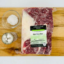 Packaged beef Dino Ribs from Creamerycreek Farms on a wooden cutting board with salt and pepper shakers.