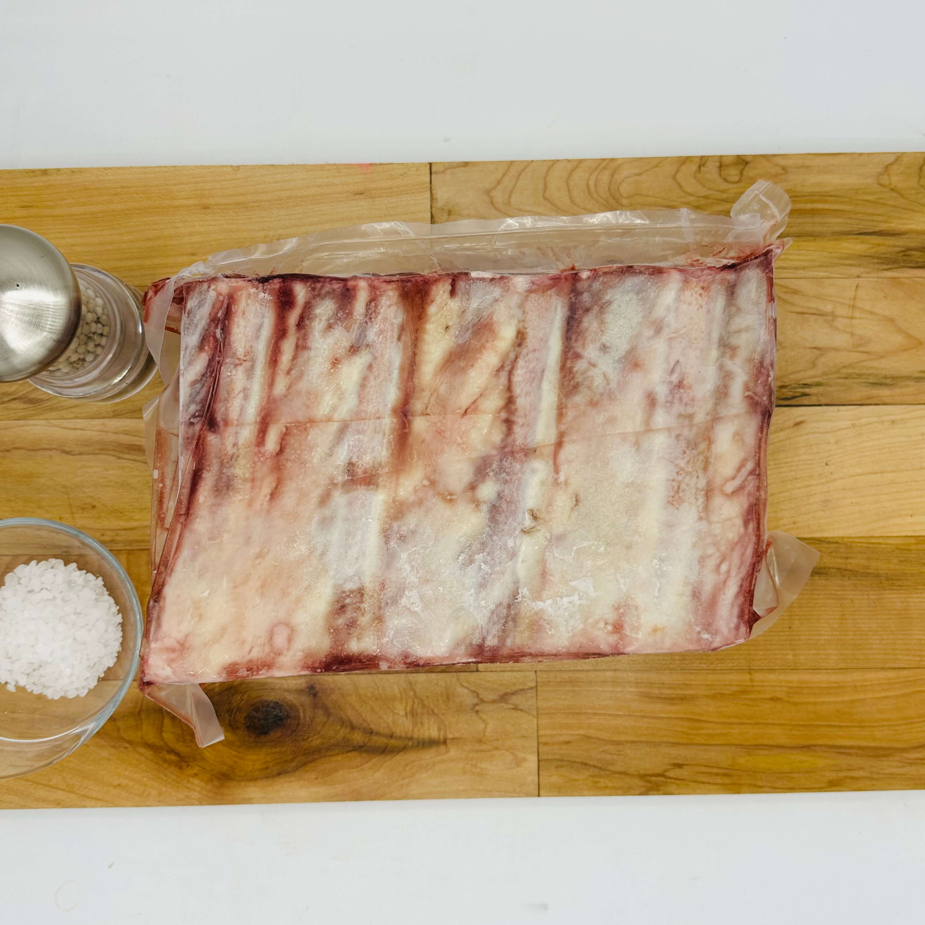 Raw meat on a wooden cutting board with salt and pepper shakers.