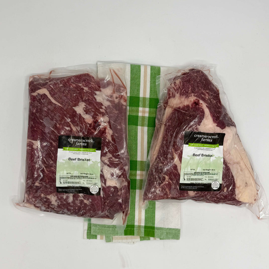 Two packages of beef brisket with Creamery Creek Farms labels on a green background.