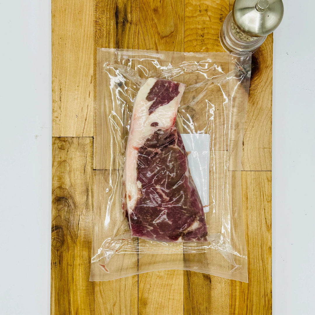 Vacuum-sealed steak on a wooden cutting board with a salt grinder.