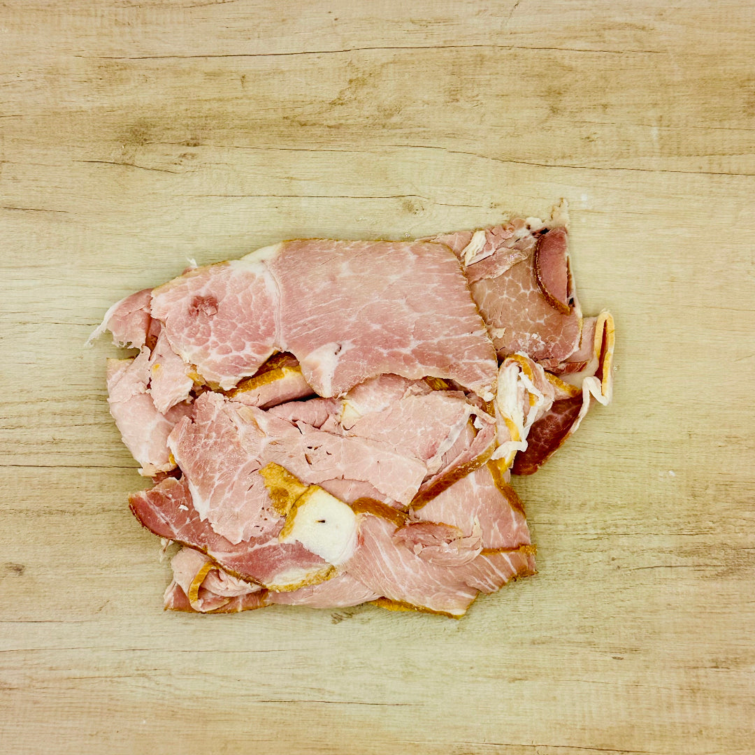 Thin slices of smoked deli ham arranged in a small pile on a light wood surface.