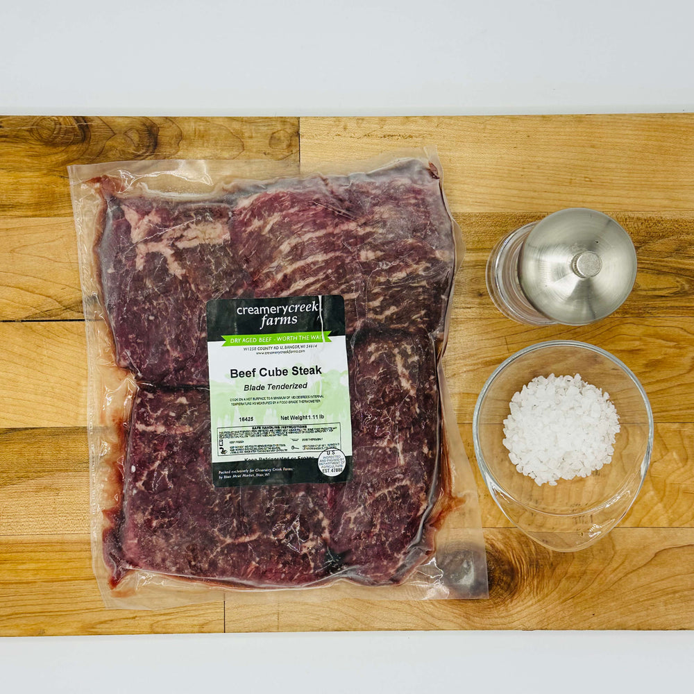 Packaged beef cube steak with a salt container on a wooden cutting board