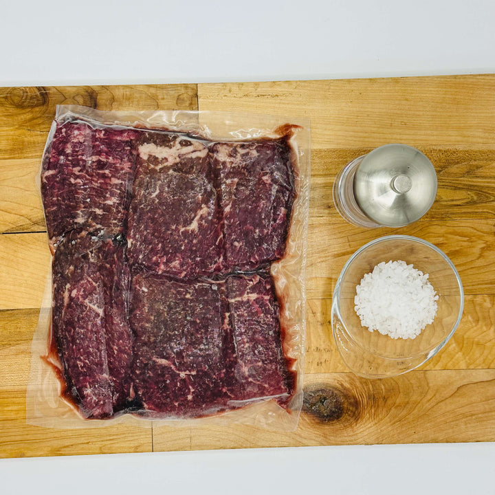 Packaged beef on a wooden cutting board with salt and pepper shakers.