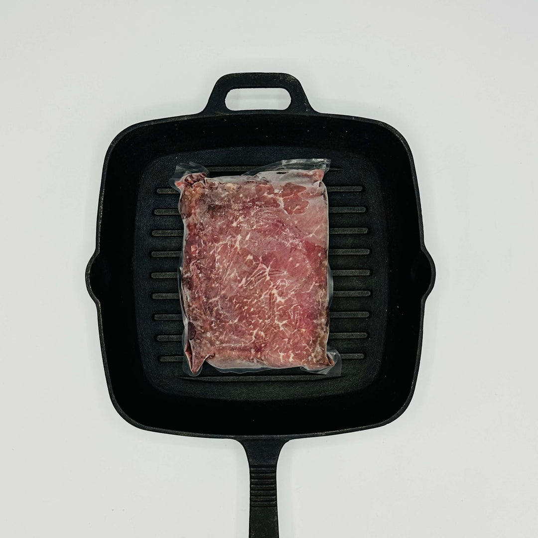 Raw steak in a plastic bag on a black grill pan with a white background