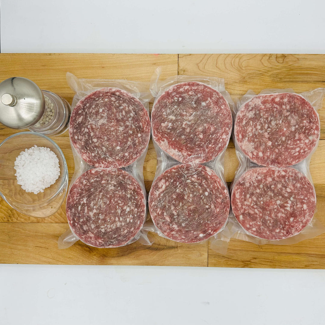 Six packages of ground meat on a wooden cutting board with salt and pepper shakers.