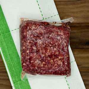 Packaged ground chuck meat on a wooden surface with a green and white towel.