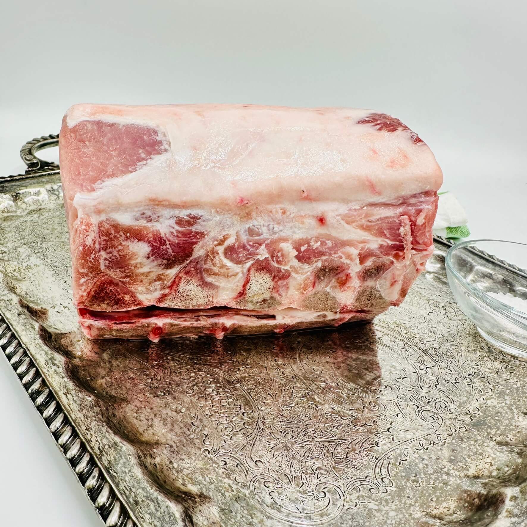 Raw pork roast on a decorative silver tray with a white background