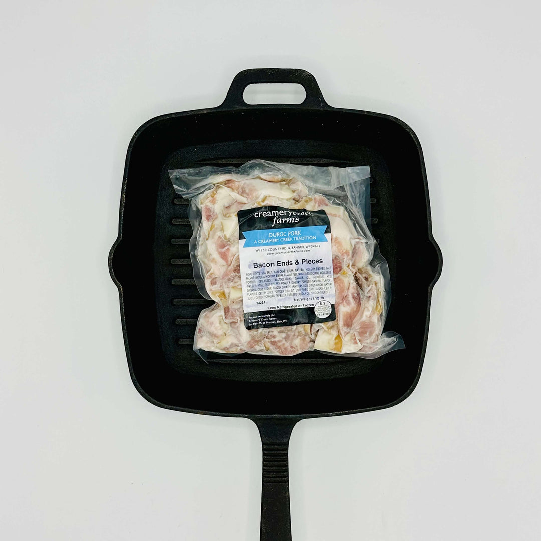 Packaged bacon ends in a black cast iron skillet on a white background