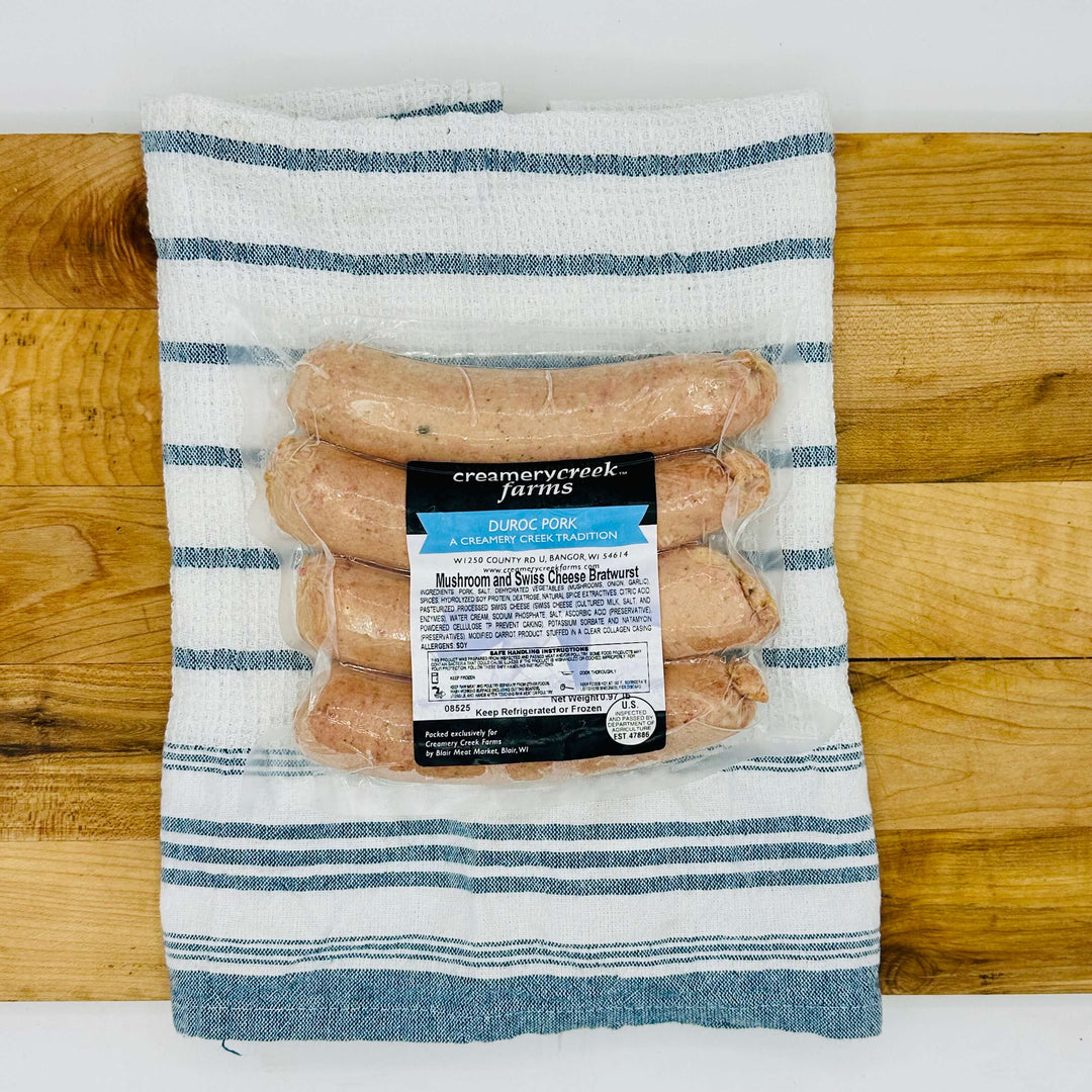 Four fresh mushroom and Swiss Duroc pork bratwursts on a tray, uncooked—extra-large size with visible inclusions and clear collagen casing, ready for grilling.