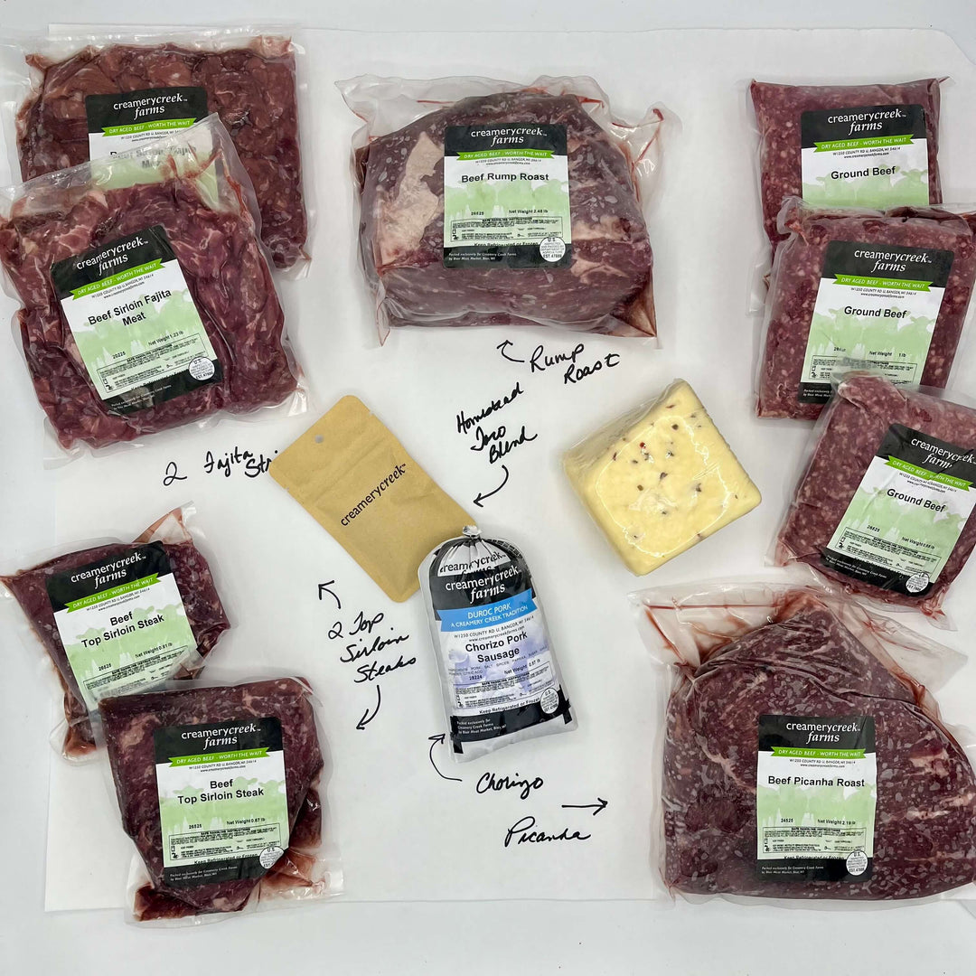 Assorted packaged meats and cheese on a white surface with 'Creamery Creek Farms' labels.