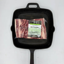 Packaged beef short ribs on a black cast iron skillet with a white background